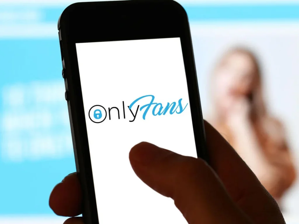 Una mujer feliz sostiene un teléfono con la aplicación OnlyFans abierta, en un entorno íntimo y sugerente.
